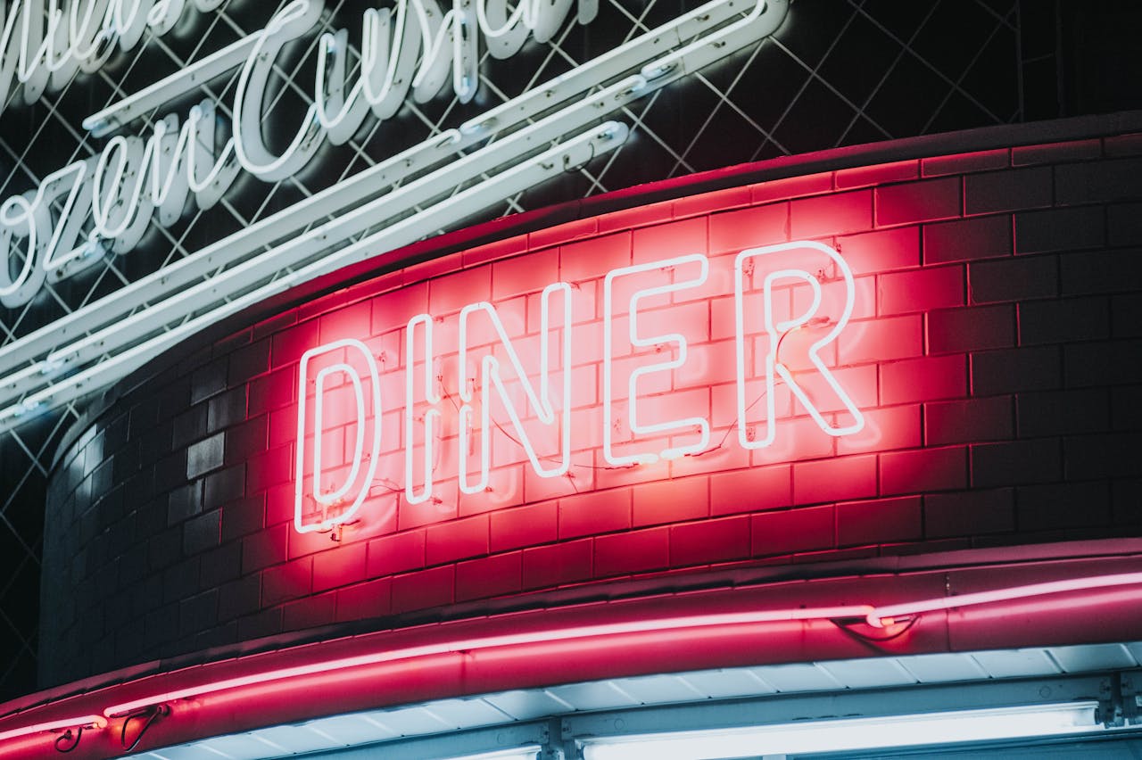 Bright neon diner sign glowing against dark tiled wall, evoking a vintage retro vibe.